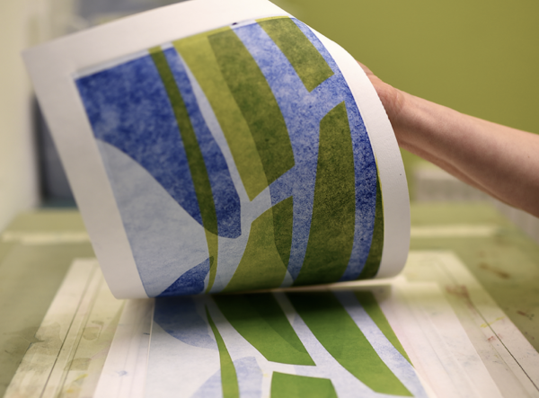 An abstract monoprint in blues and greens being lifted from the plate