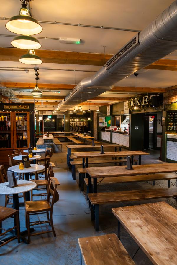 A view down the length of the venue, with low wooden tables and benches, and small round quartzz-effect tables to one side.