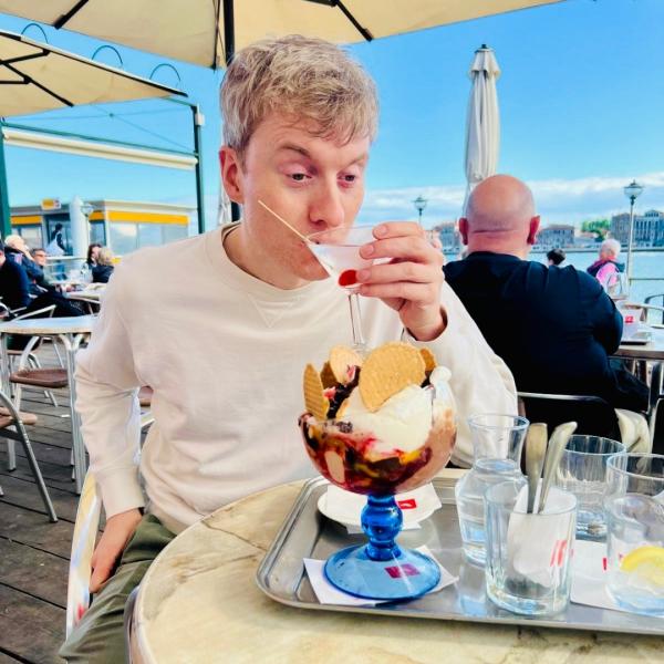 James Acaster sips a martini at a beach-front restaurant.