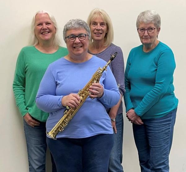 Four delightful looking ladies smiling for camera, one is holding a saxomophone