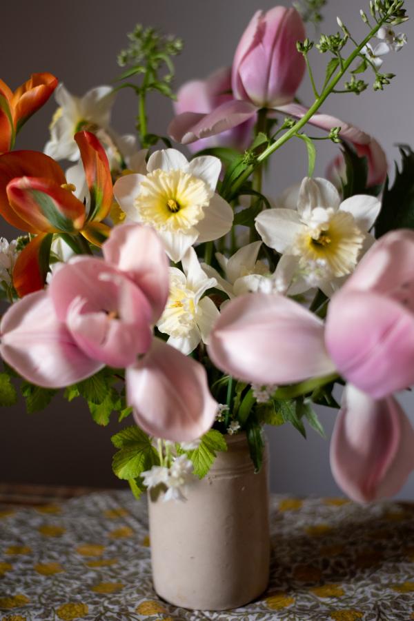 Imagge shows daffodils, tulips and other spring flowers in a victorian jam jar on top of a table cloth