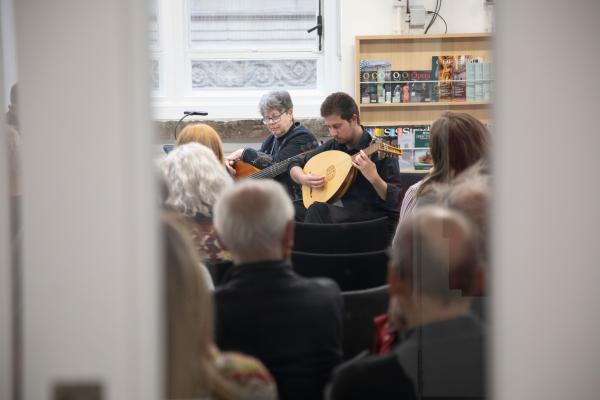 Person playing lute in crowd of people image taken through doorway