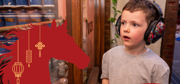 Young boy in Abbey House Museum wearing ear guards, next to a symbol of a horse.