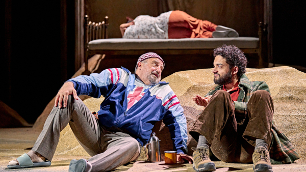 Two actors performing on stage. They are both sat on the floor.