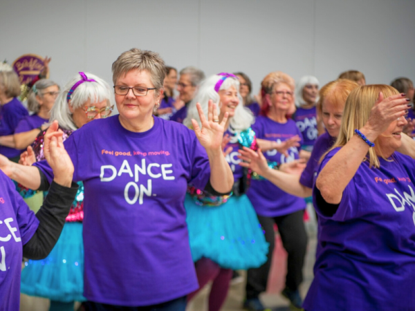 A group of women in 'dance on' T-shirts are dancing together 
