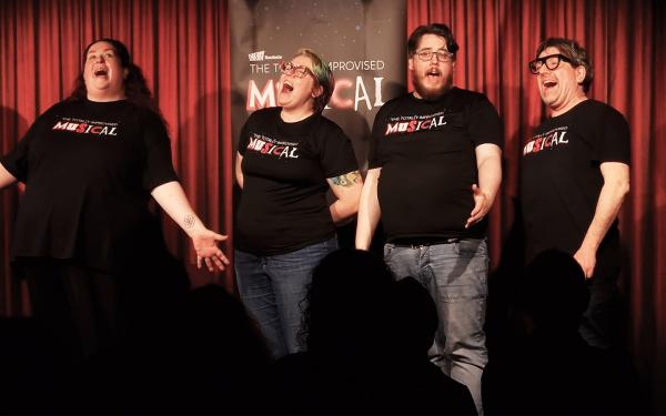 The Totally Improvised Musical cast singing a group number against a red curtain.