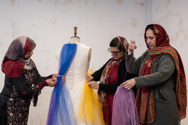 Three women in headscraves, sewing tulle to a mannequin boddess 