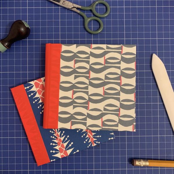 A photograph of two handmade notebooks on a blue cutting mat