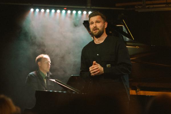 James Newby sings on a stage in front of Joseph Middleton playing piano