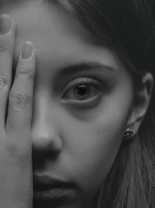 A girl covering an eye with her hand. In black and white.