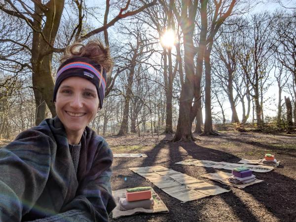 a woman smiling in a woodland surrounded by yoga mats
