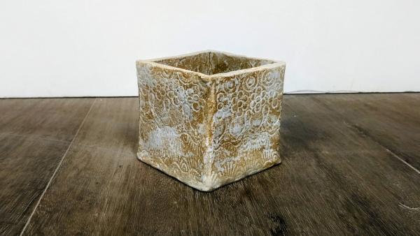 A photograph of a beige and white ceramic open top box on a wooden table