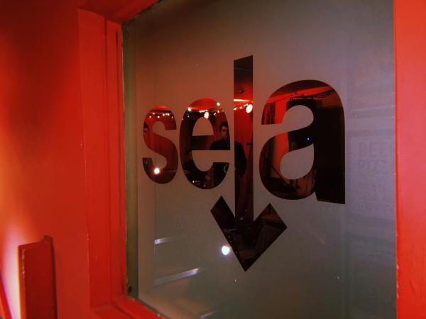 Photograph of 'sela' logo in a red lit window.