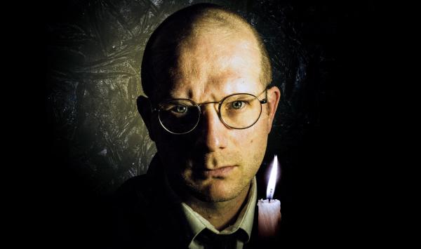 A sinister looking man with a shaved head and round spectacles stares moodily into the camera, a solitary candle lights the scene, I hope he's acting I wouldn't like to think of anyone looking like that otherwise