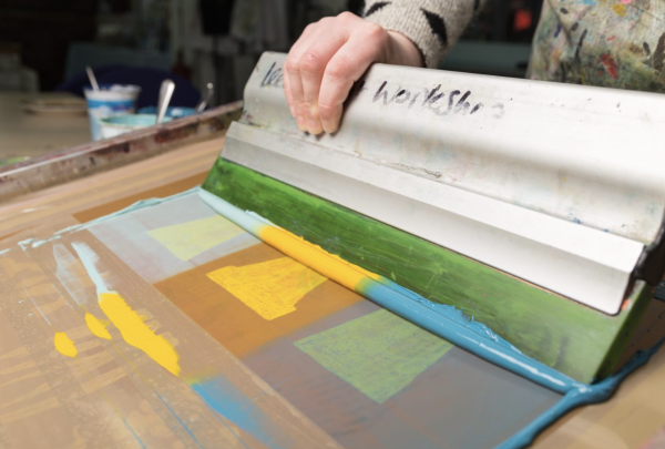 A squeegee being used to screen print an image of plant pots in shades of blue and yellow ink