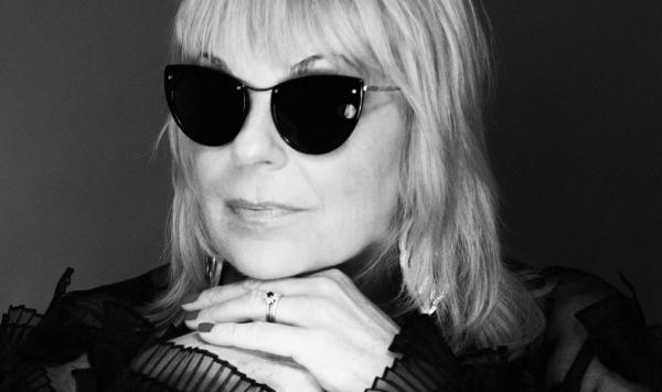 Black and white portrait of a lady with shoulder length blonde hair, she is wearing sunglasses even though she's indoors