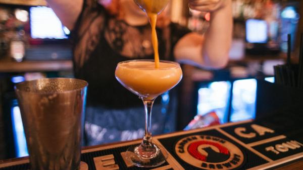 A close up shot of a cocktail being strained into a coupe glass.