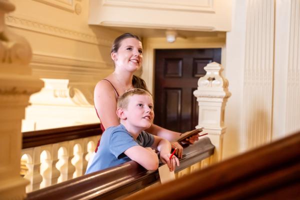 A woman and a young boy smiling over the bannister at Lotherton Hall, each holding a pen and paper.
