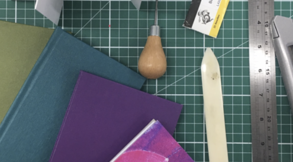 Hand bound books in various colours, alongside a selection of bookbinding tools