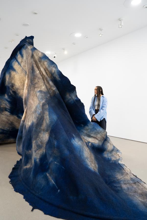 A visitor stands next to a large felt freestanding sculpture in blue and white, resembling a mountain or crashing wave