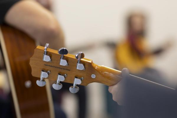 Tuning pegs of a guitar in focus, blurred figures of guitar players in the background.