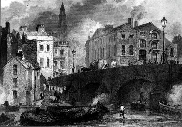 Image of an old stone bridge with buildings behind it and the spire of a church.