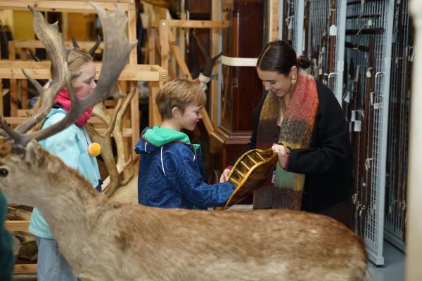 Two children at a Store Tour with the tour guide, taking a closer look at one of the objects in the collection..