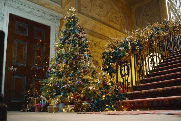 A decorated Christmas tree at the bottom of a grand staircase in a stately home.