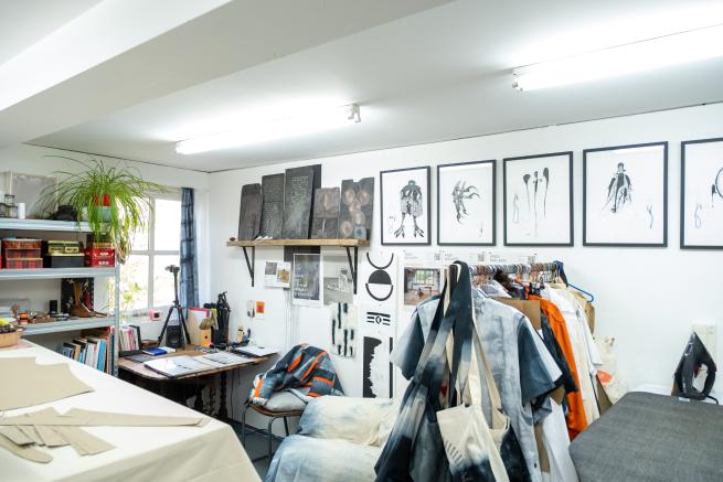 An artist studio can be seen, with textiles hung on a clothes rail, and images hung along a white wall