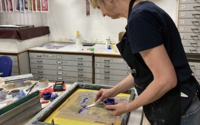 An artist adding ink to a screen in a print studio