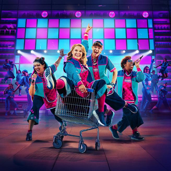 Promotional image for Here & Now. Four singing and dancing characters in matching blue and pink supermarket uniforms, as one of them sits in a moving shopping trolley, in front of neon lights and backing dancers. 