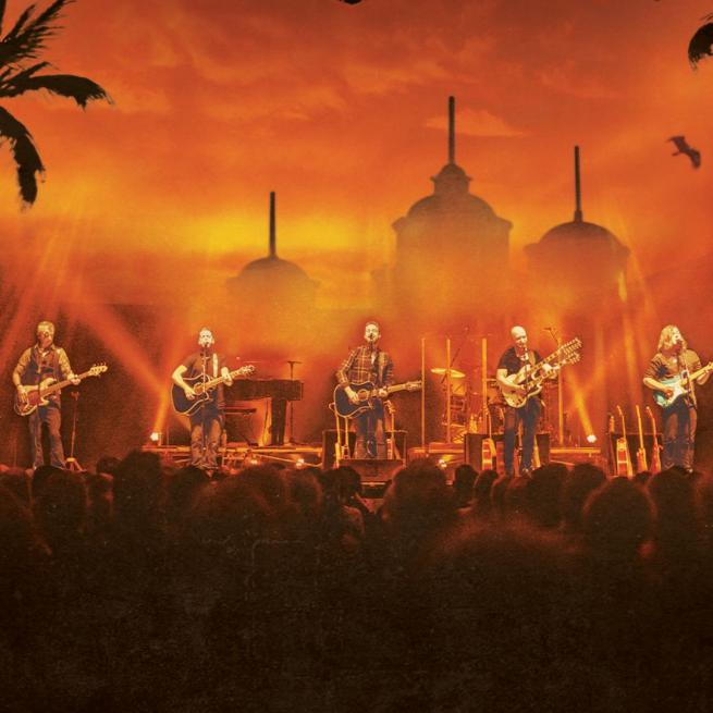 In front of a hazy, deep orange skyline of buildings, palm trees and a soaring eagle, six guitarists perform on stage to a crowd.