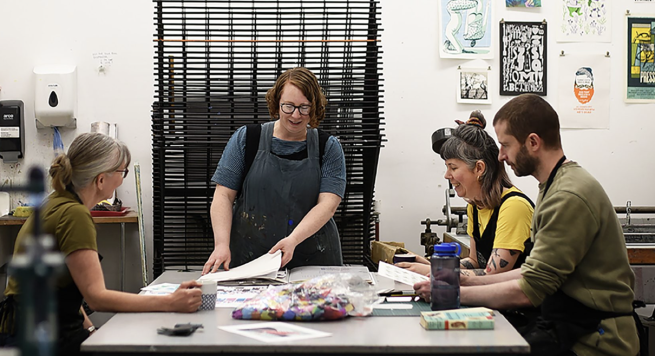 Four artists sat around a table in a print studio discussing their work 