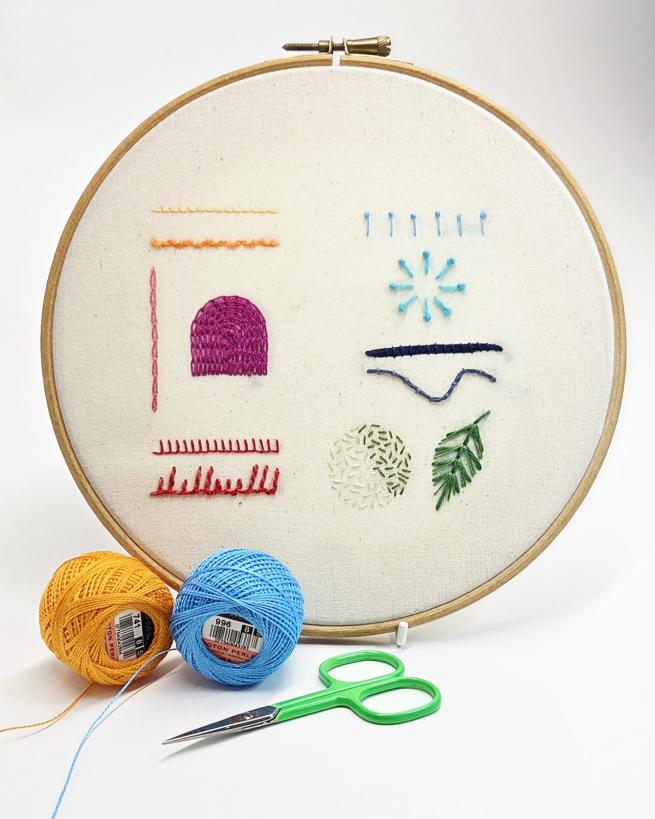 An embroidery hoop with various embroidery patterns, besides some thread spools and a pair of scissors