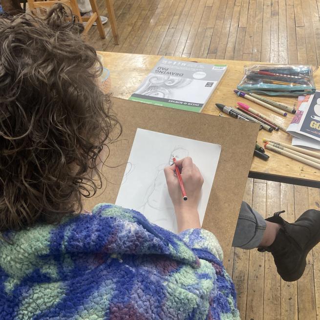  A photograph taken over a persons shoulder as they are drawing a figure on a piece of white paper
