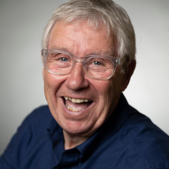 Gregor Fisher smiles at the camera in front of a plain grey background.