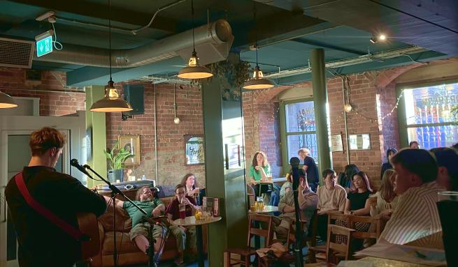 A person is playing guitar with their back to the camera, a crowd is watching.