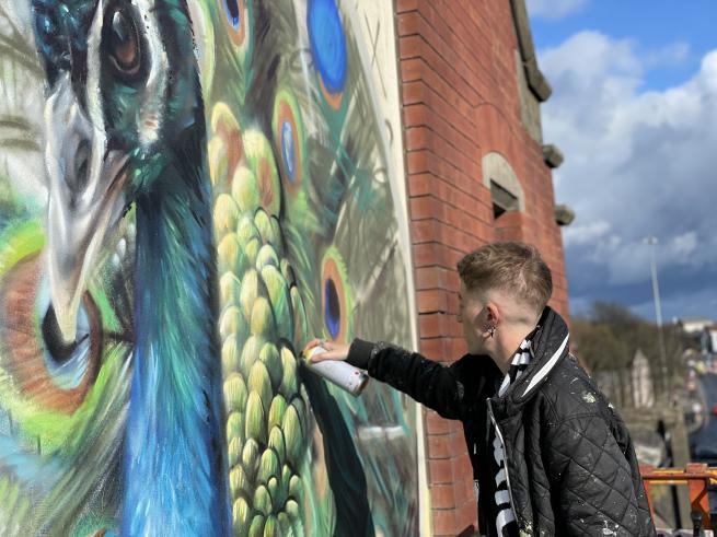 Artist CBLOXX painting a mural on a red brick wall