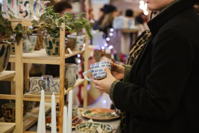 A woman holding a blue and white patterned ceramic mug over a stall covered in Clod Studio pottery