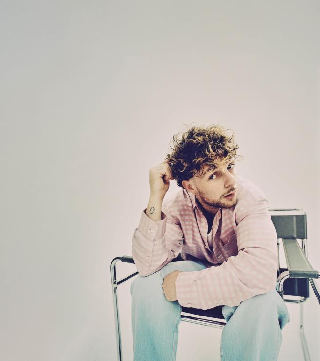 Tom Grennan seating on a chair looking straight at the camera