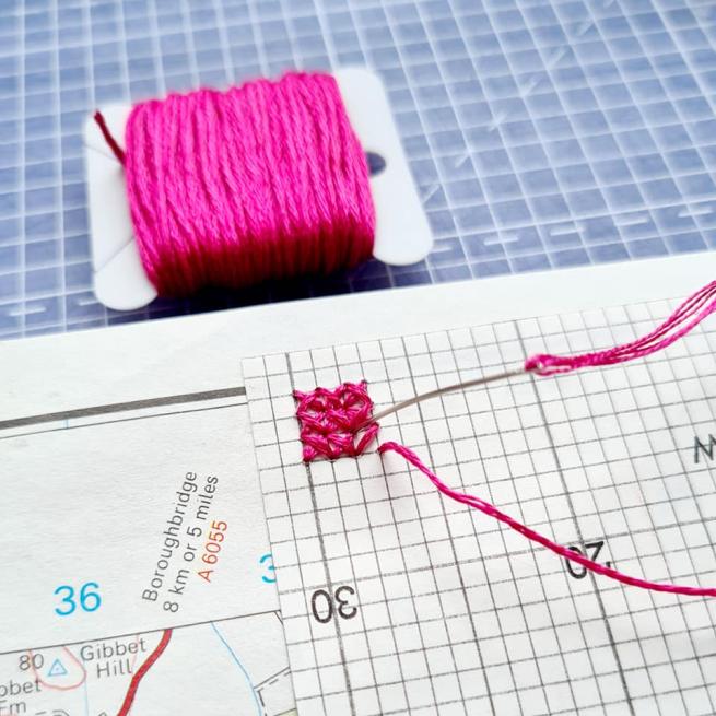 Pink thread being embroidered into patch squares.