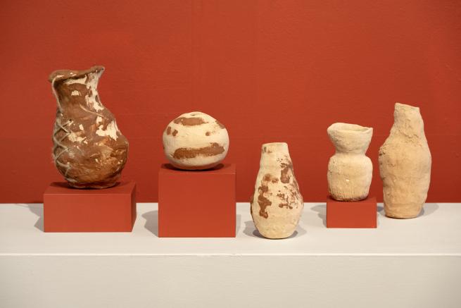 Hand built clay pot on white and red plinths with a red wall background