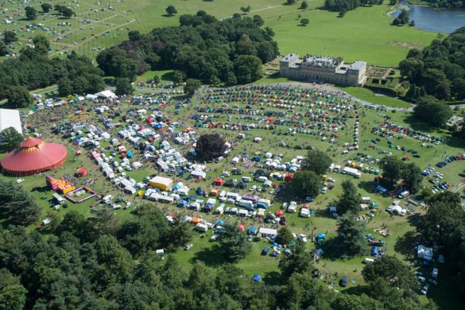 a birds eye view of a large field filled with tents, cars and food stalls 