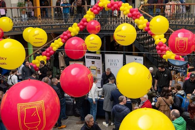 Suspended Red and Yellow large balloons with a red and yellow balloon garland over groups of people sampling whisky