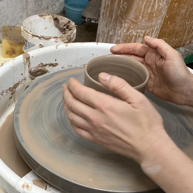 Two hands throwing a ceramic vessel on the wheel