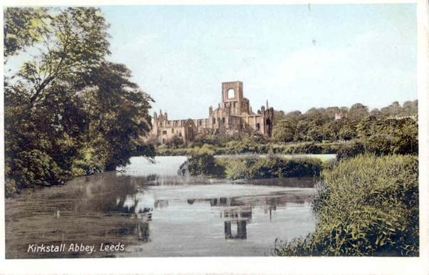A tinted colour photograph of a river and trees with a ruined monastery in the background
