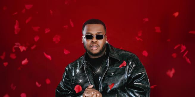 A person wearing a black leather jacket and sunglasses. The background is red with rose petals