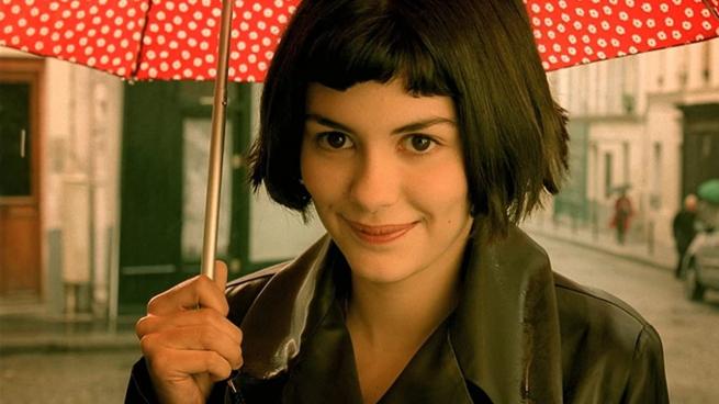 A young woman with a short dark bob cut, smiling mischievously and holding a red spotted umbrella. 