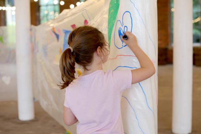 young child draws on plastic stretched out in old mill space 