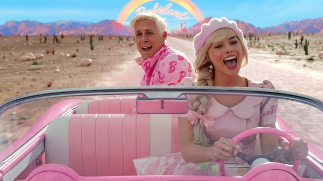 Barbie drives down a desert road in a bright pink convertible, Ken sits in the back. Both of them are singing. 